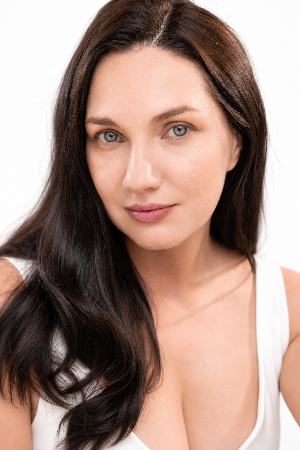 Woman with long dark hair wearing a white tank top on a white background