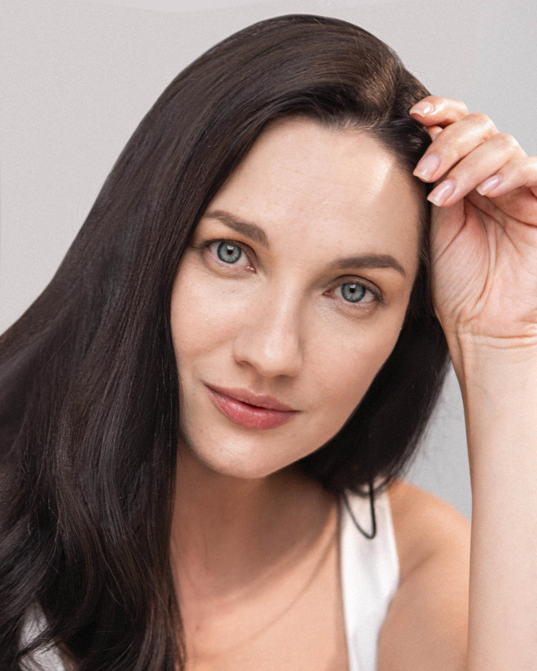 Woman with long dark hair touching her head against a neutral background