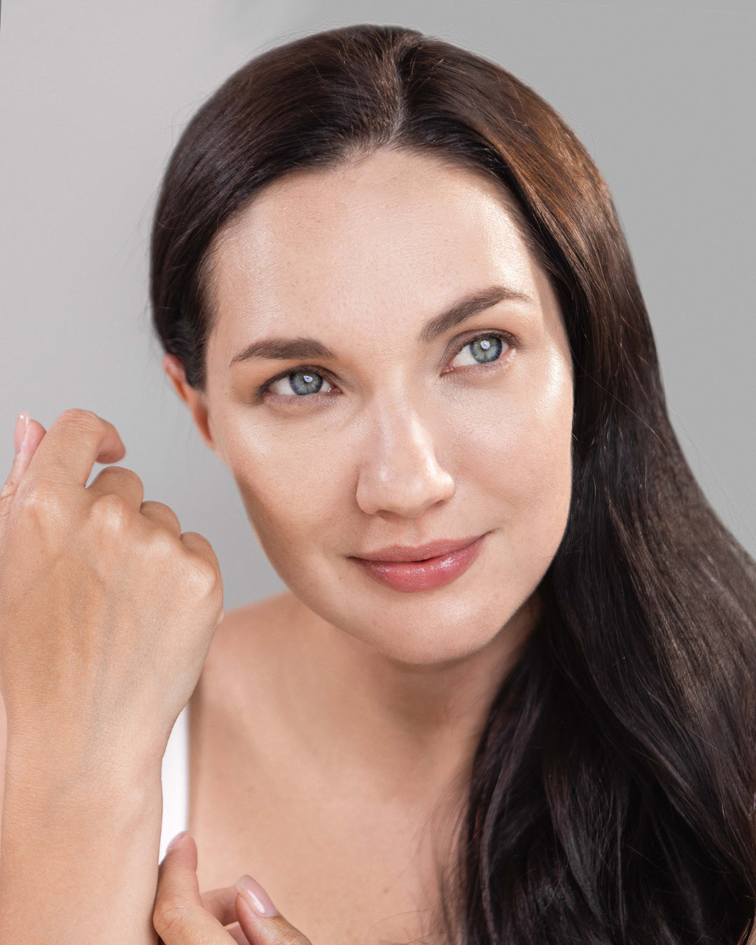 Woman with long brown hair and clear skin against a gray background