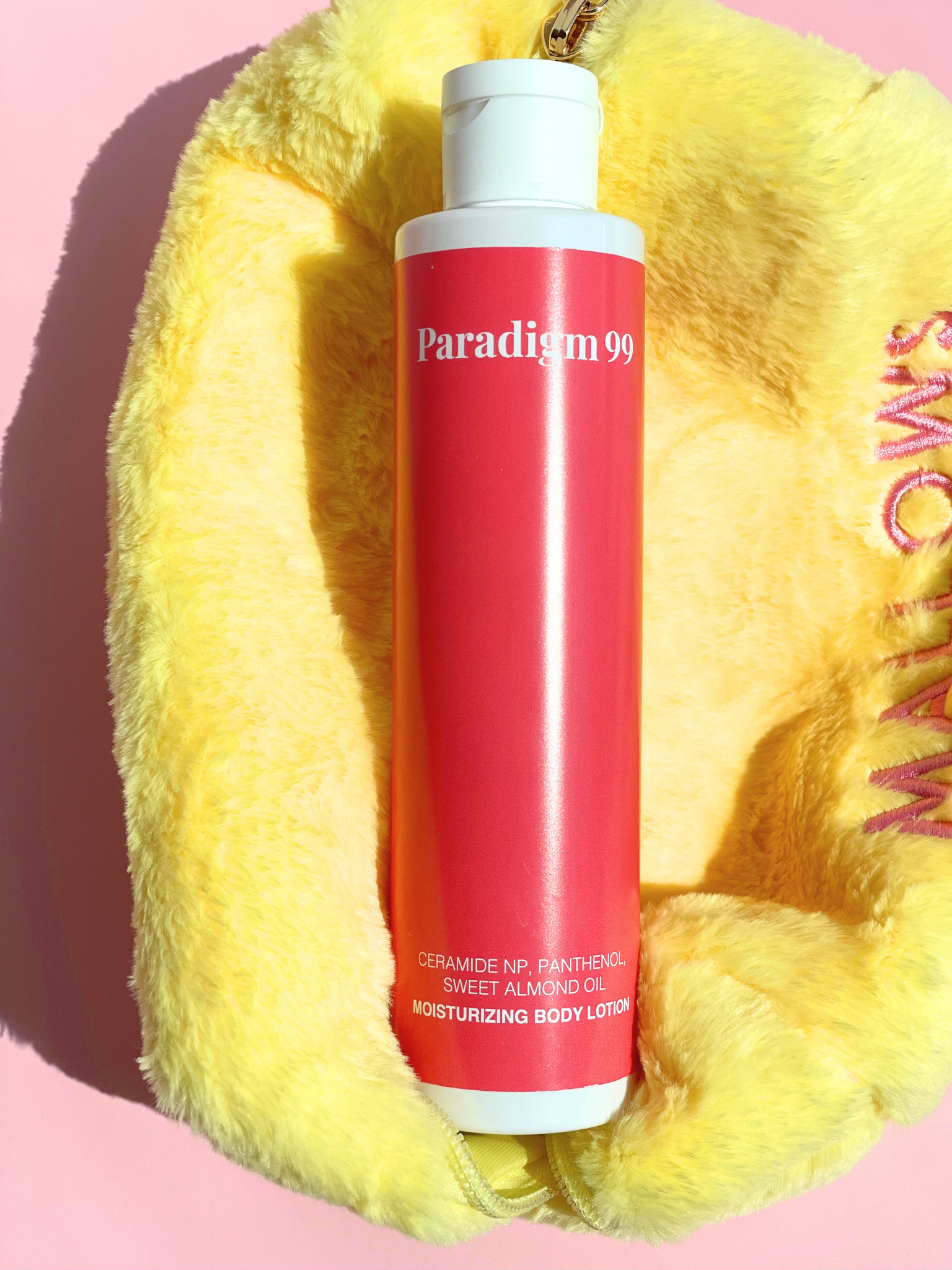 Body lotion bottle labeled 'Paradigm 99' on a yellow textured surface with pink background.