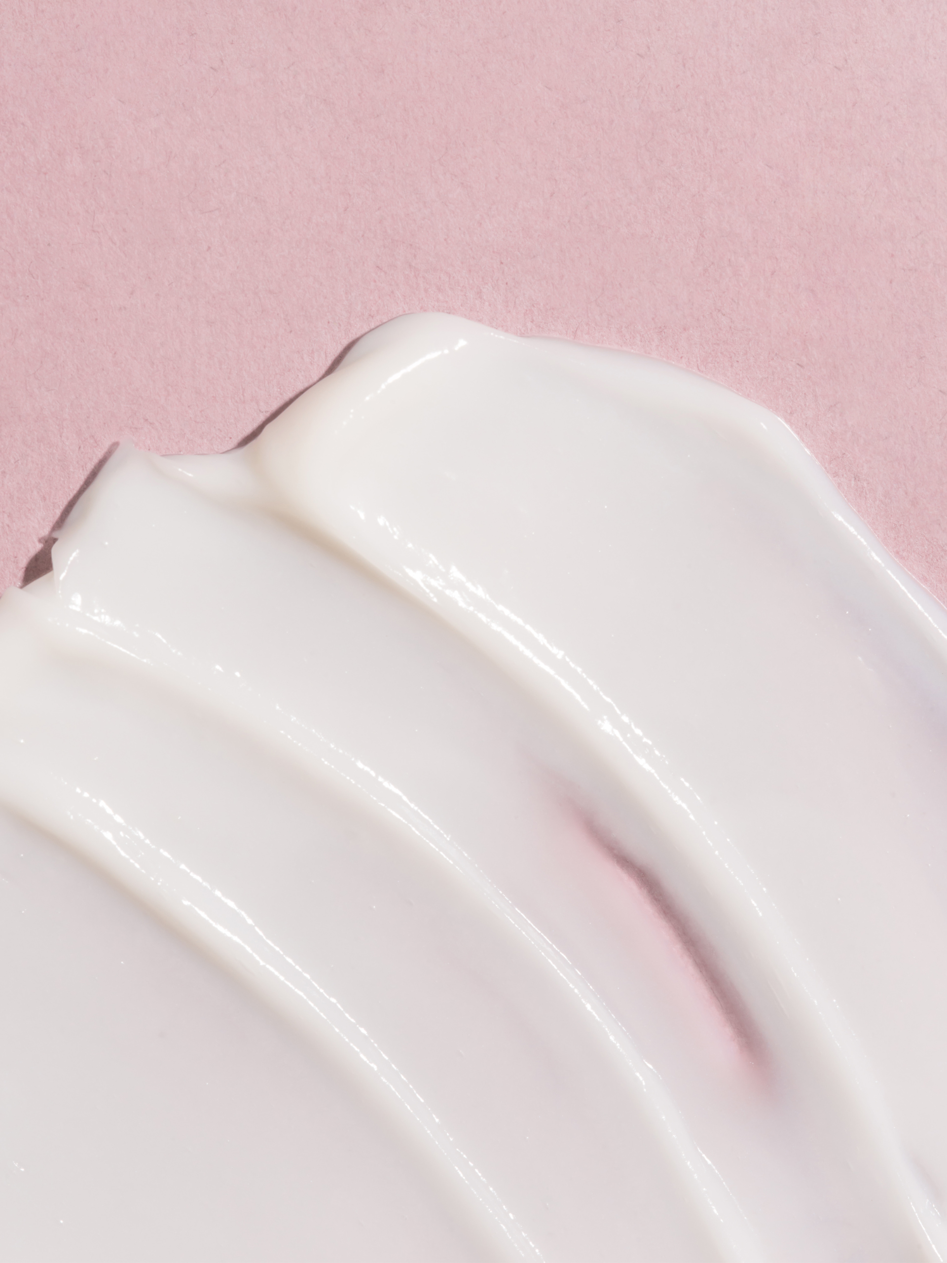 Close-up of a smooth, white moisturizing body lotion swatch on a pink background. 