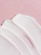 Close-up of a smooth, white moisturizing body lotion swatch on a pink background. 