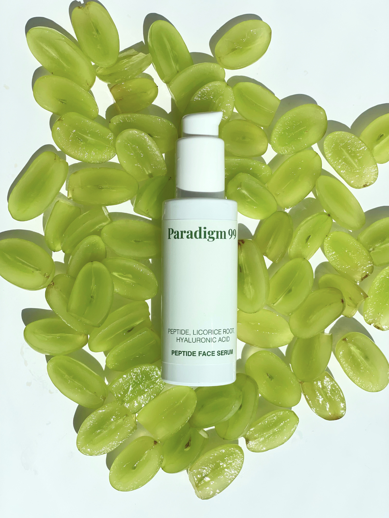 Paradigm skincare peptide serum bottle surrounded by green grapes on a light gray background.